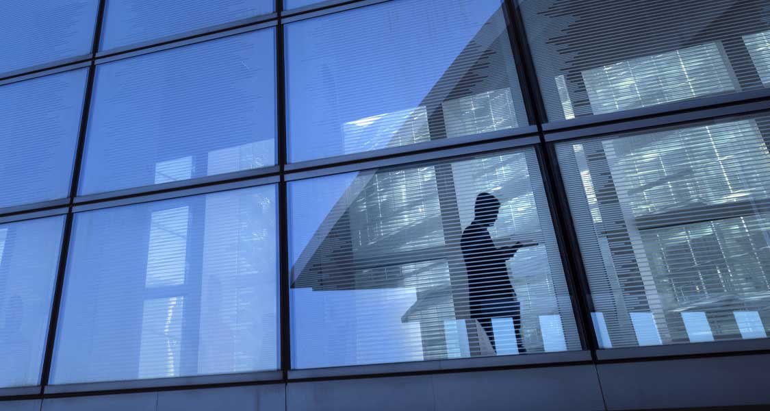 A businessman looking at his mobile phone in the hallway of a tall, glass building